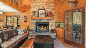 A cozy living room with a stone fireplace, leather sofa, and a mounted deer head. - New! Riverfront Retreat - Sleeps 12, Ellijay (Ellijay)
