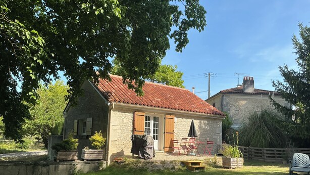 Una cabaña de piedra con tejado de tejas rojas, una puerta de madera y un pequeño patio con mobiliario exterior.