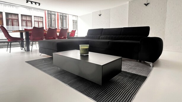 A modern living room with a black sectional sofa, a glass coffee table, and red chairs. - Discover our unique design loft in downtown Mons (Mons)