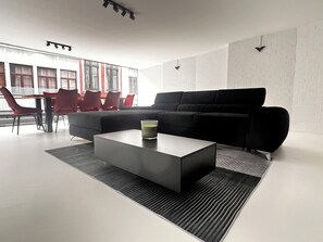 Un salon moderne avec un canapé d’angle noir, une table basse en verre et des fauteuils rouges.