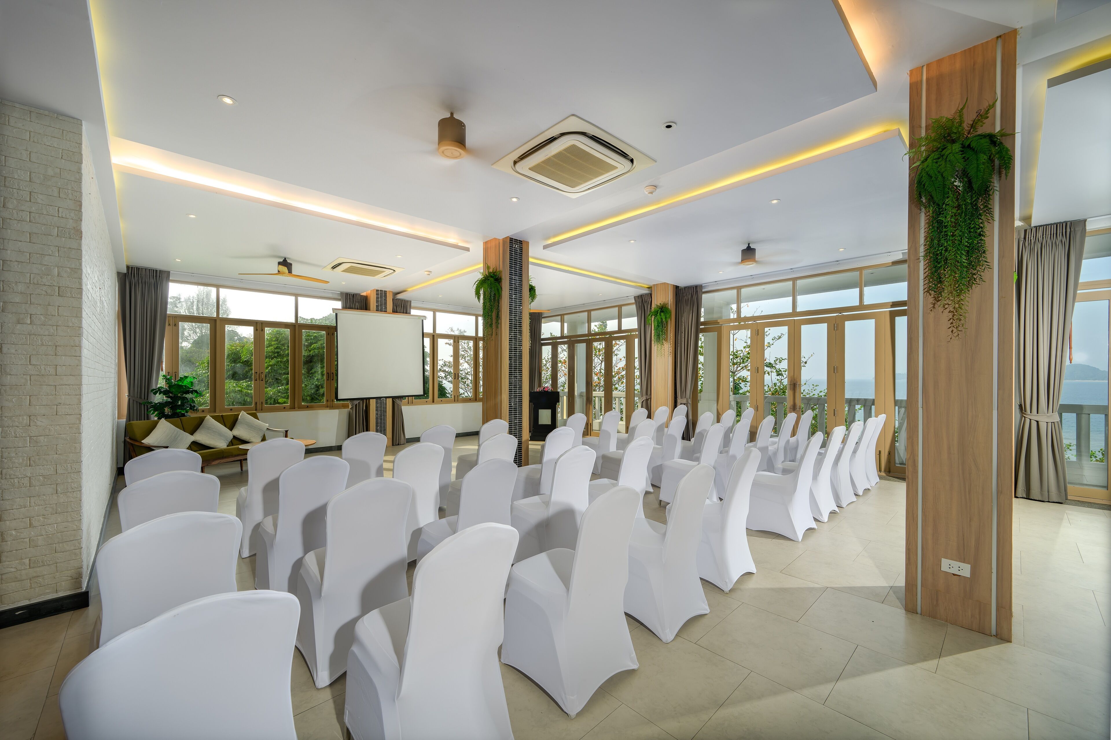 A conference room with rows of white chairs, a projector screen, and large windows.