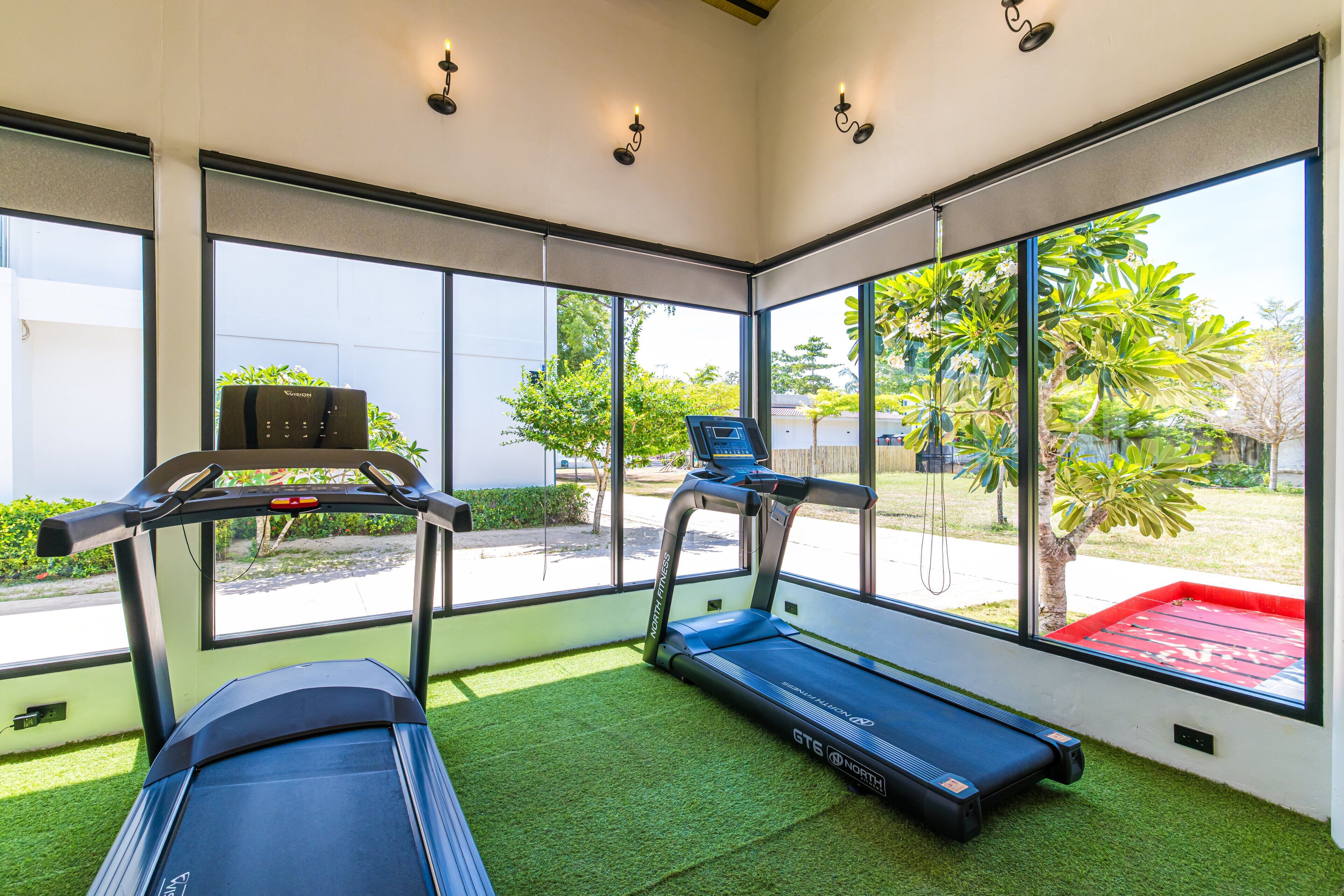 A gym with treadmills and a stationary bike, large windows, and artificial grass flooring.