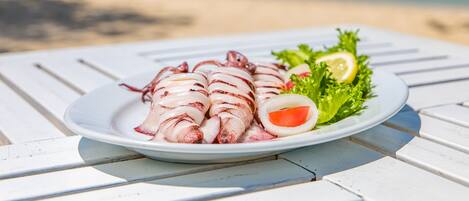 Une assiette de calamars grillés, servis avec du citron et de la laitue, sur une table blanche au bord de la plage.