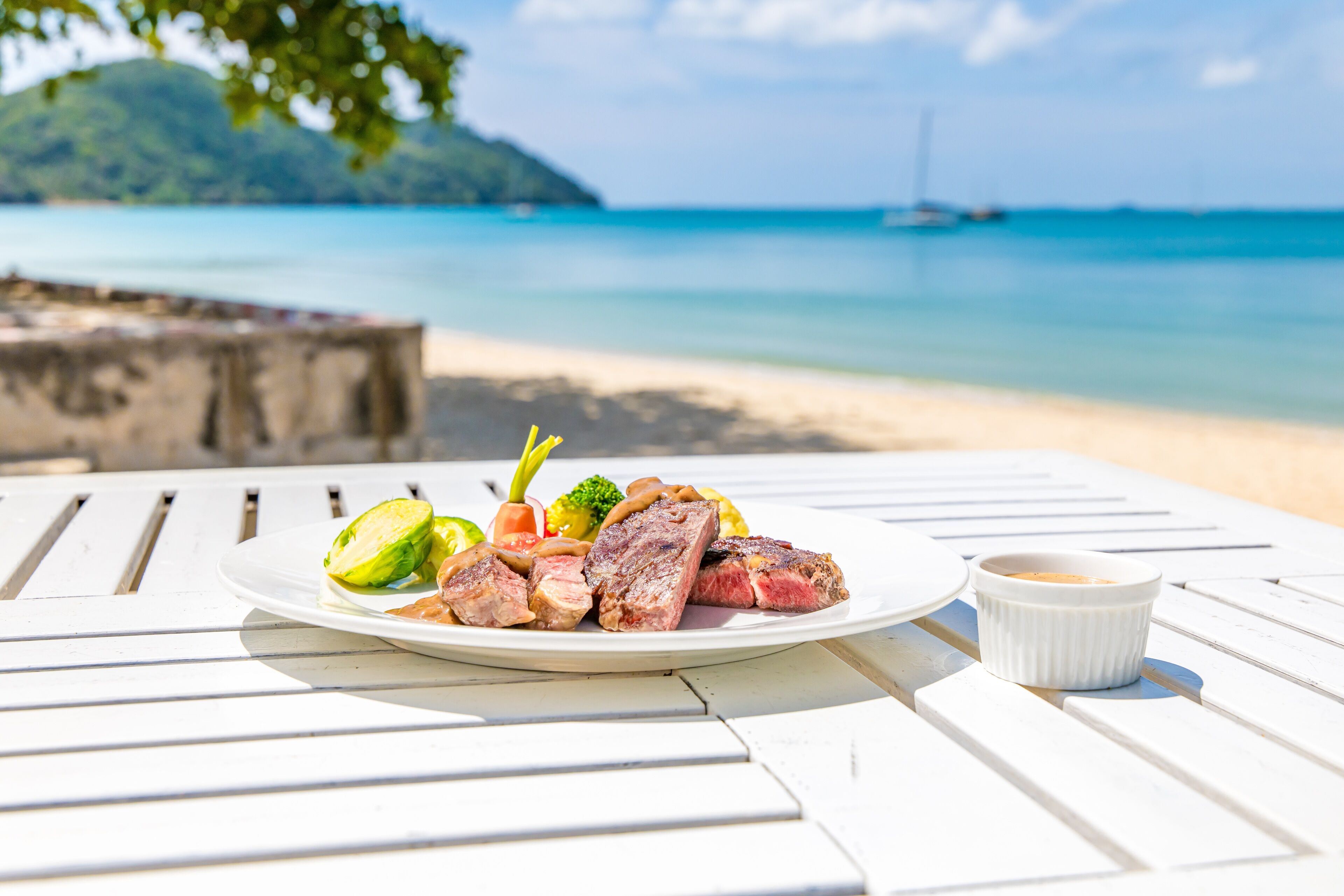 Un plato de comida sobre una mesa blanca, con vista a una playa y al océano al fondo.