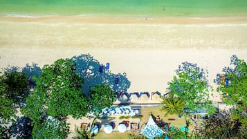 An aerial view of a beach with clear turquoise water, a sandy shore, and a row of blue umbrellas and lounge chairs.