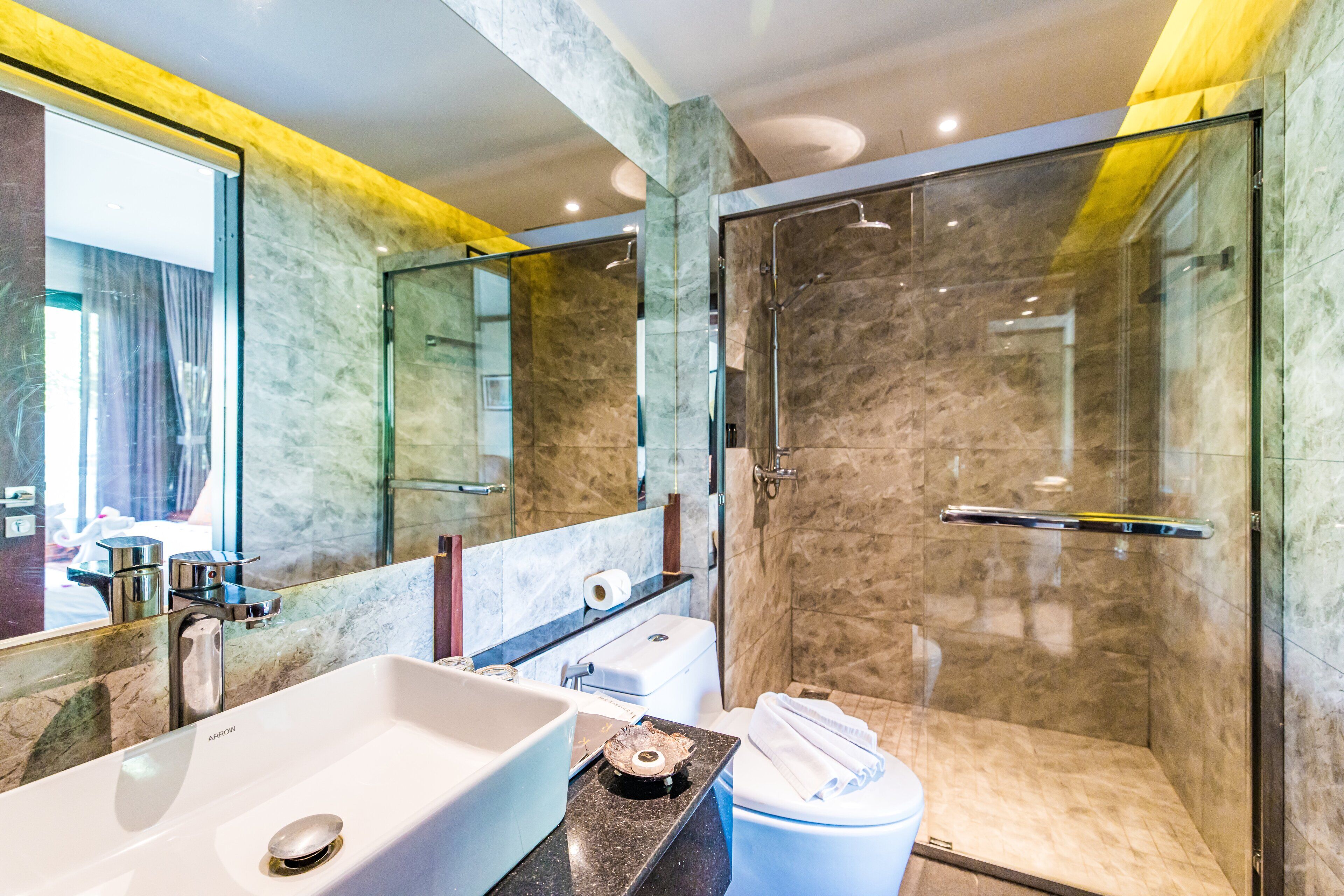 A modern bathroom with a large mirror, a sink, a toilet, and a glass-enclosed shower.