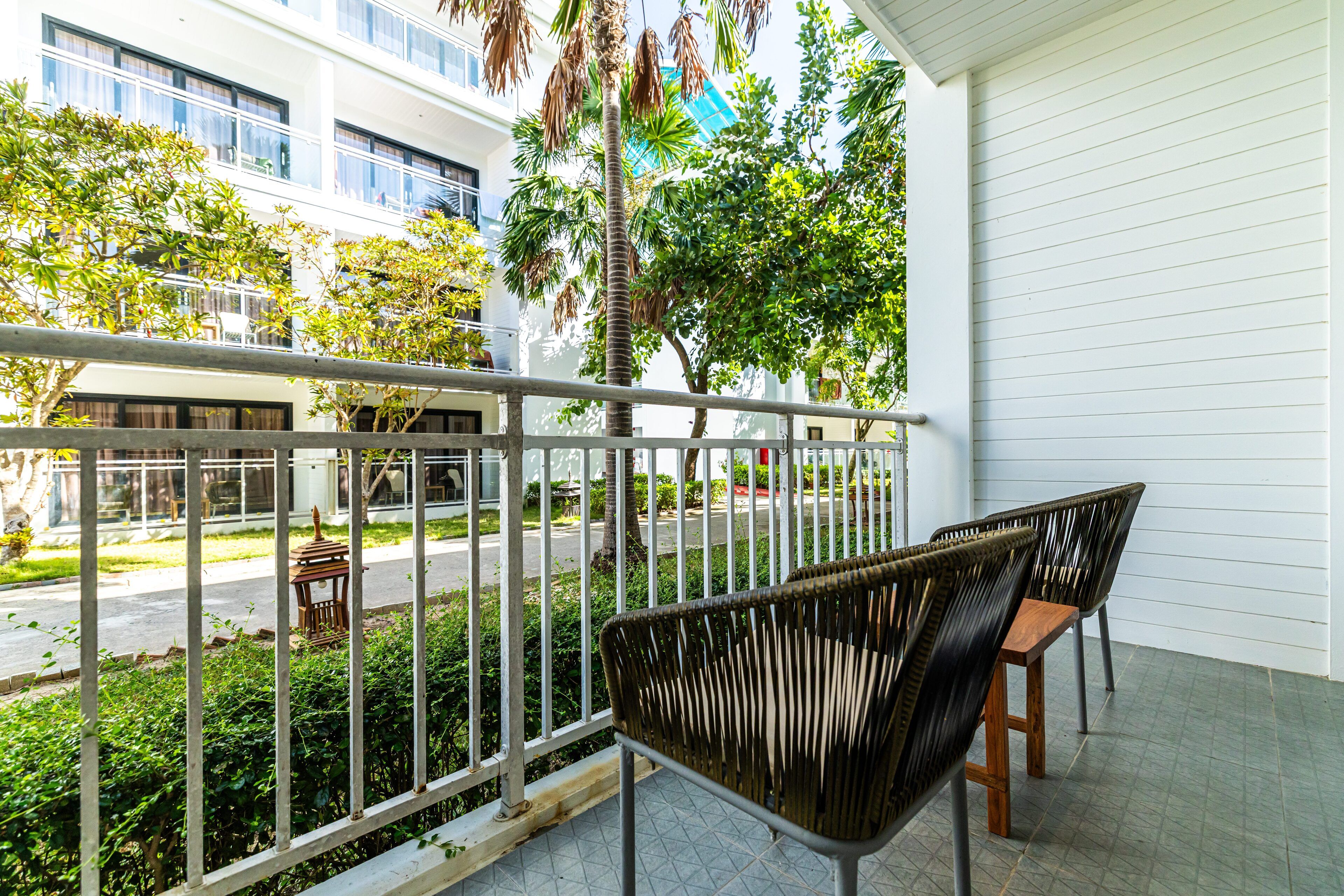 A balcony with wicker chairs, a railing, and a view of a street and buildings.
