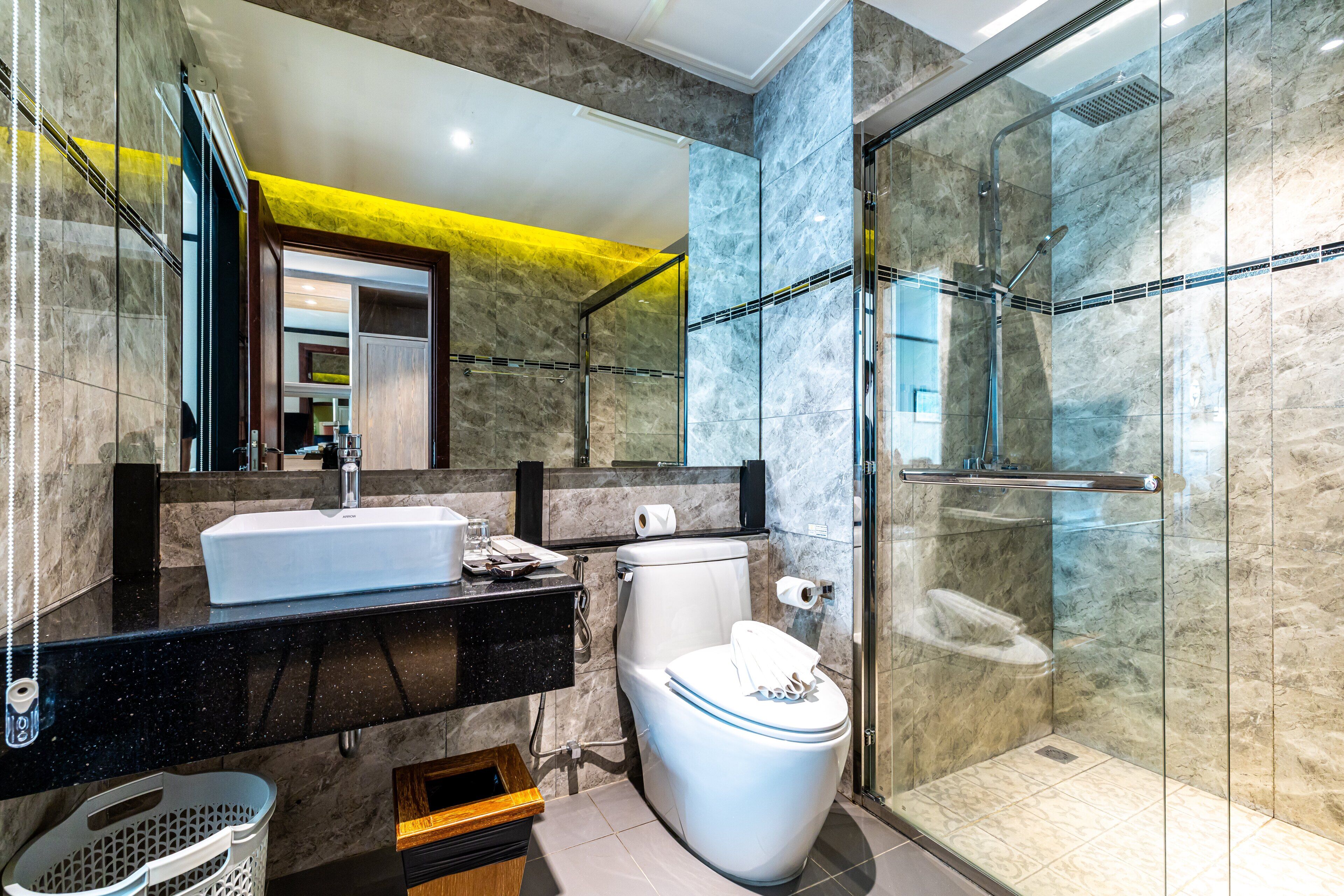 Un baño moderno con ducha envuelta en vidrio, inodoro blanco y encimera negra con lavabo.