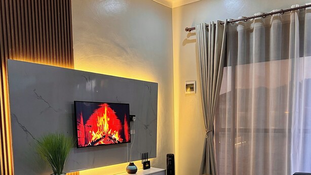 Una sala de estar moderna con un televisor de pantalla plana mostrando una chimenea, un sofá, una mesa de centro y una planta en maceta.