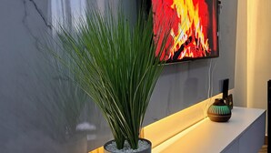 Una sala de estar moderna con un televisor de pantalla plana montado en la pared, una planta en maceta sobre una consola blanca y un jarrón decorativo.