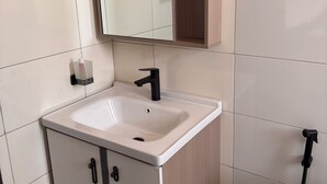 Un baño con un lavamanos blanco, un espejo, un armario y un perchero para toallas.