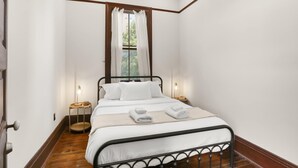 Une chambre avec un lit simple, une fenêtre avec des rideaux, des lampes de chevet et un plancher en bois.
