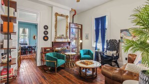 Un salon doté d’un plancher en bois, de fauteuils turquoise, d’un canapé en cuir marron, d’une table d’échecs et d’un ventilateur de plafond.
