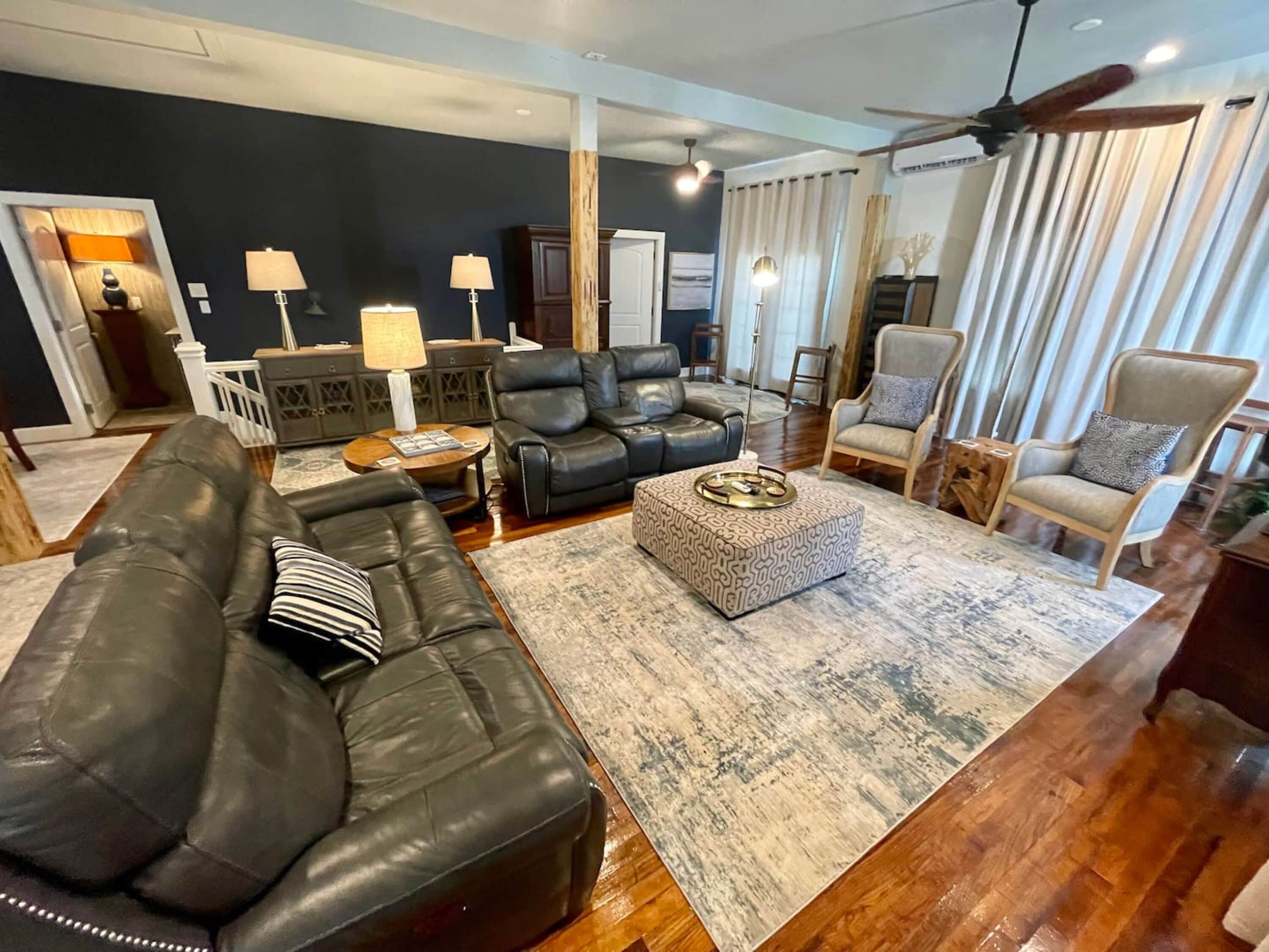 A living room with a dark wall, leather sofas, a patterned ottoman, and a ceiling fan.