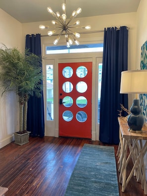 A room with a red door, a ceiling light fixture, a potted plant, and a lamp on a wooden table. - Coastal Retreat Near Pleasure Pier & Beach (Galveston)