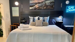 Un lit bien fait, avec des oreillers et des serviettes pliées, un téléviseur fixé au mur, une enseigne au néon et un tableau encadré au-dessus du lit.