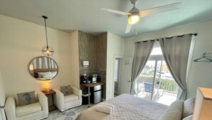 Une chambre d’hôtel équipée d’un lit, d’un canapé, d’un bureau avec une machine à café, d’un ventilateur de plafond et offrant une vue sur l’extérieur.
