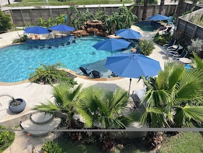 Ein Schwimmbecken mit mehreren Sonnenschirmen, Liegestühlen und Palmen.