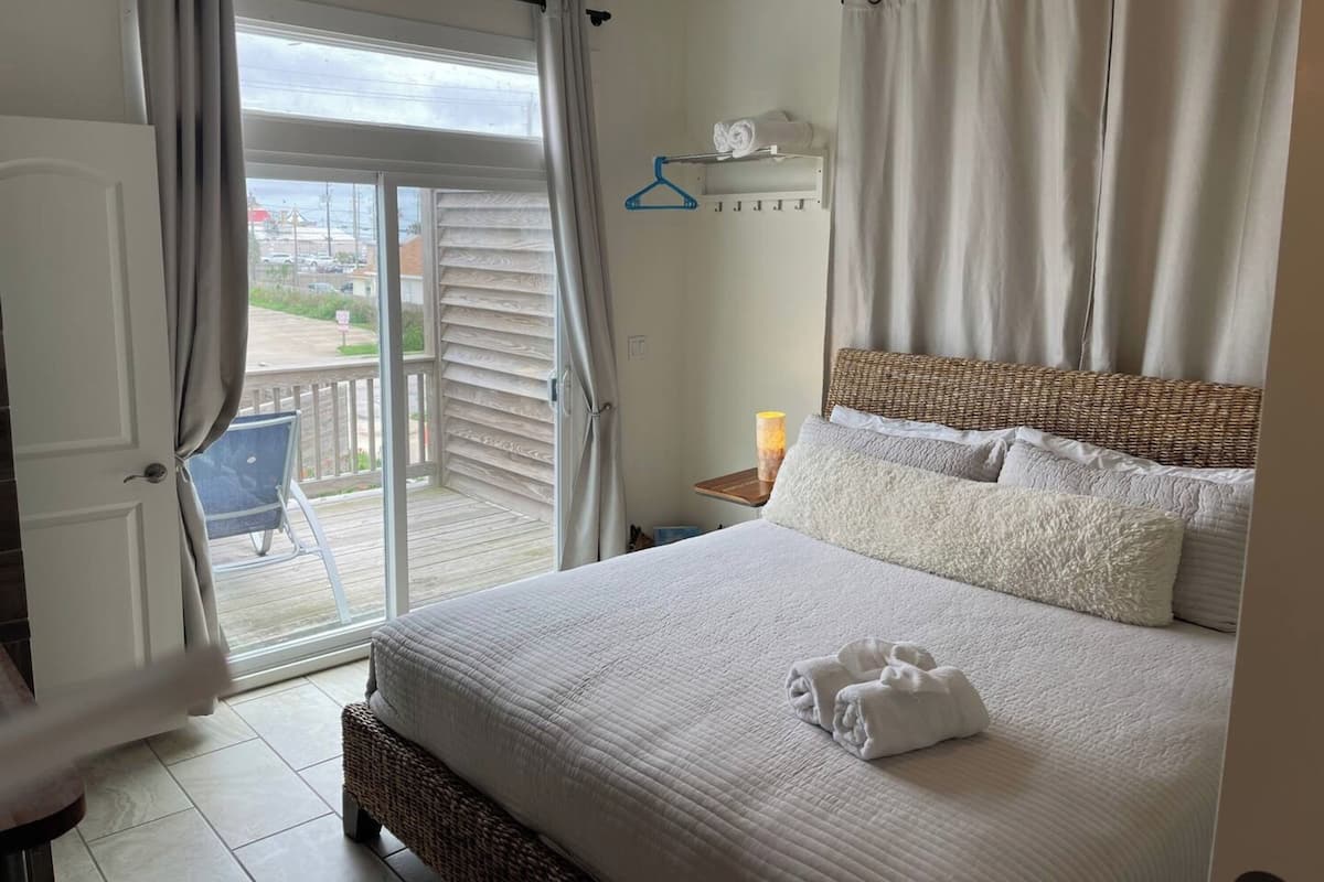 Une chambre avec un grand lit, un balcon avec une chaise et une vue sur l’extérieur.