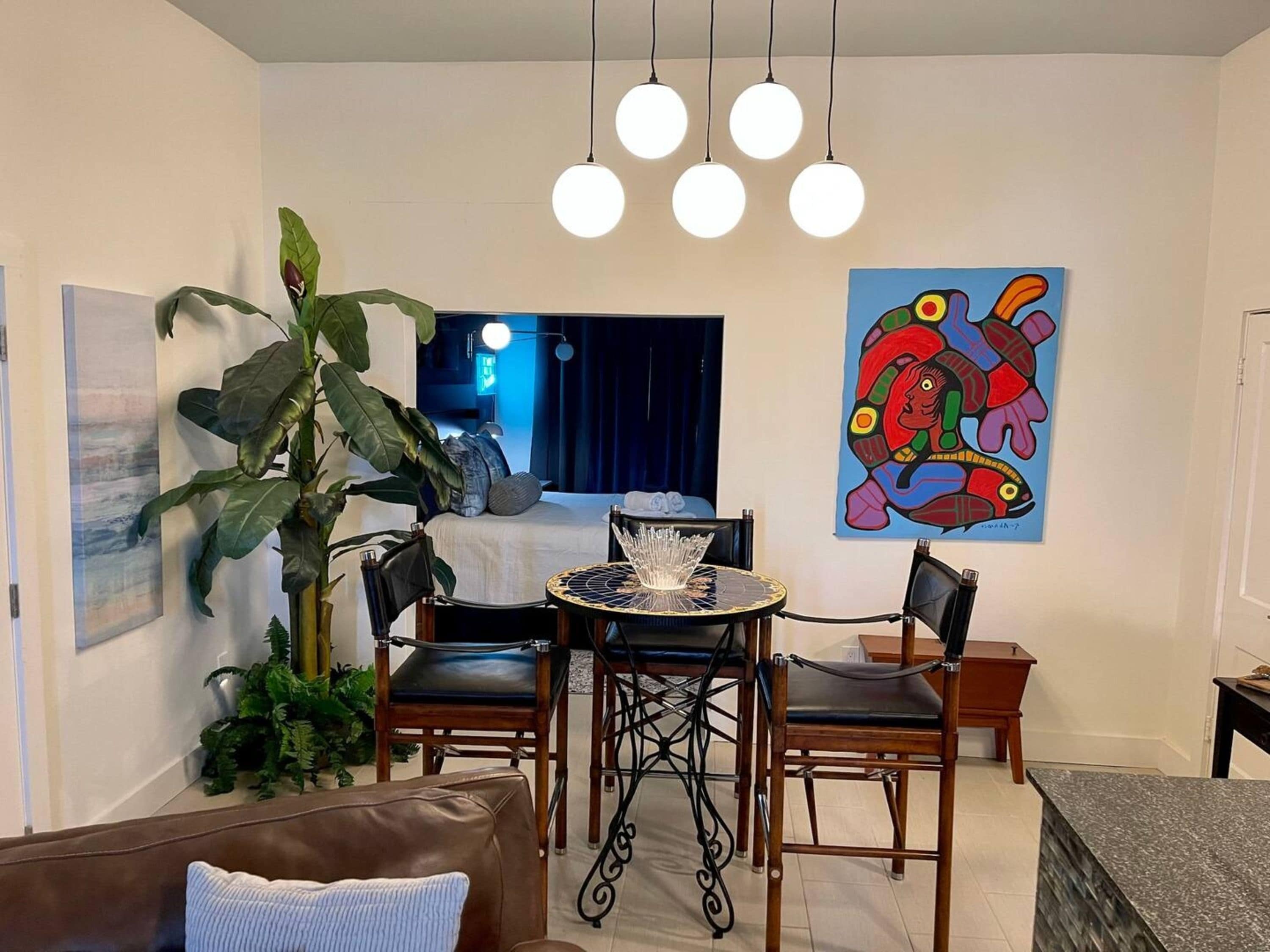 A modern living room with a dining area, a large plant, and a colorful artwork on the wall.