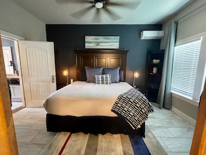 A bedroom with a bed, a ceiling fan, a painting, an air conditioner, and a window with blinds. - Coastal Retreat Near Pleasure Pier & Beach (Galveston)
