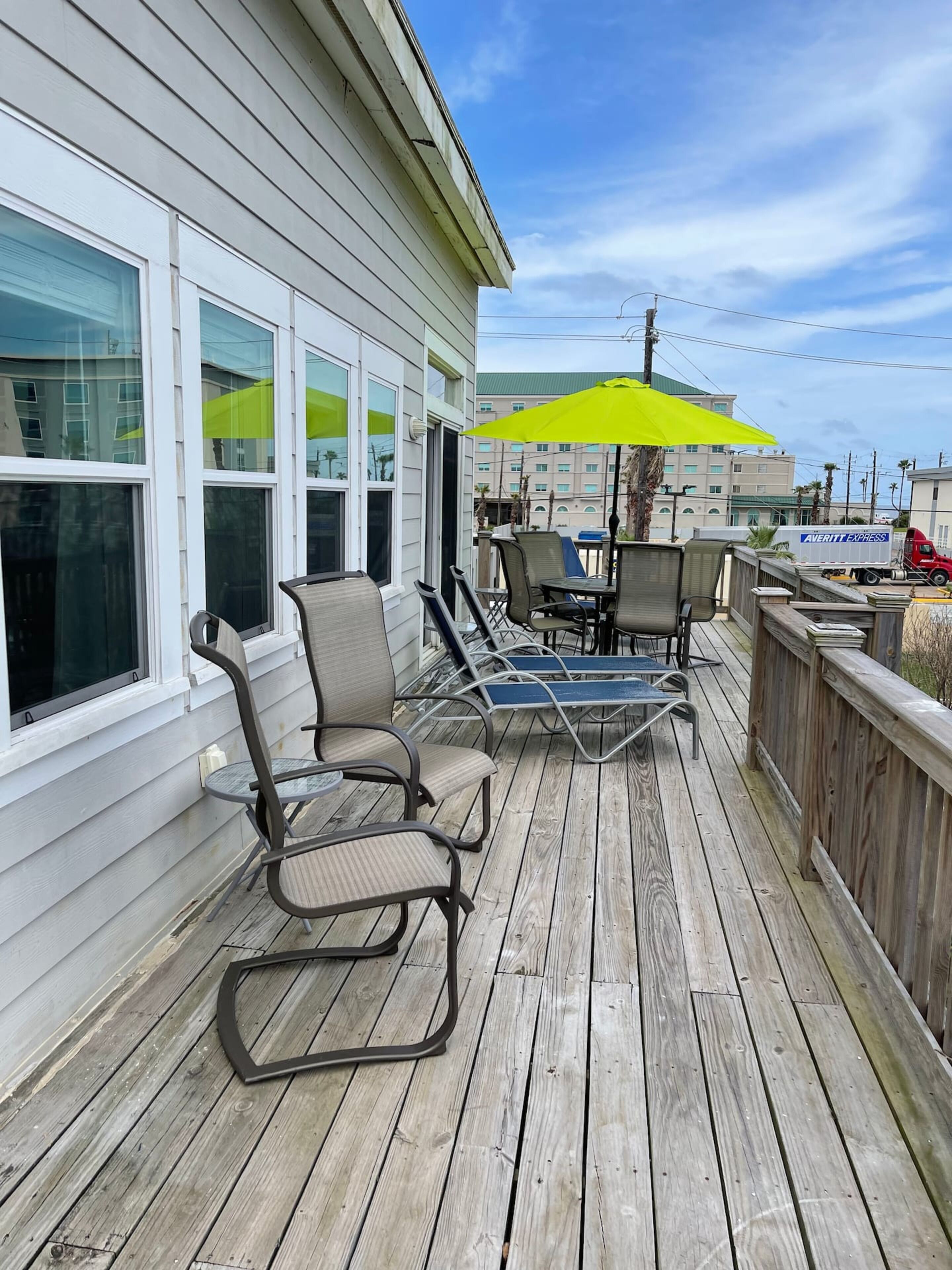 A wooden deck with outdoor furniture, including chairs and a table, and a bright yellow umbrella.