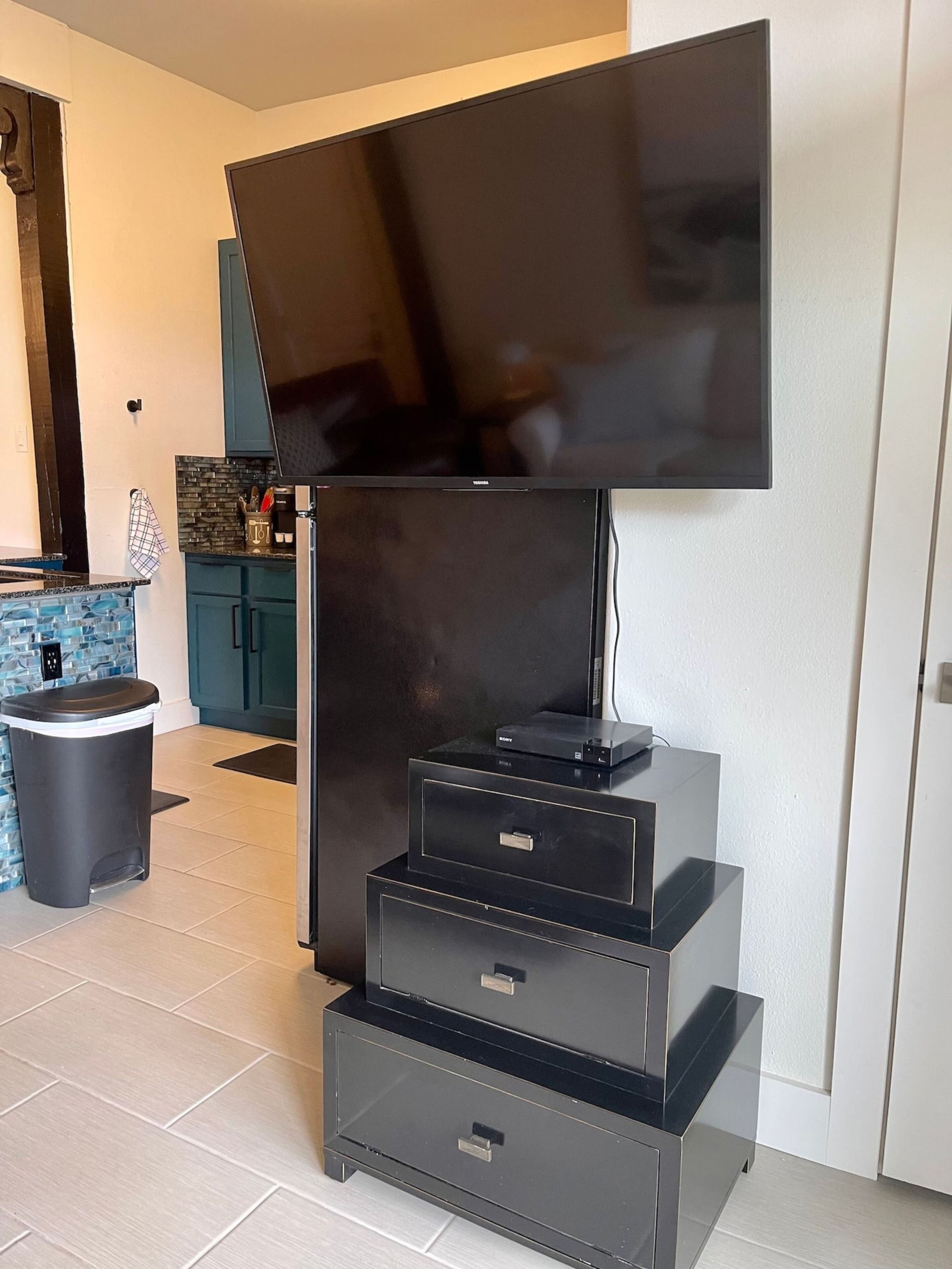 Cozinha moderna com televisão de tela plana em suporte, lixeira e painel de azulejos.