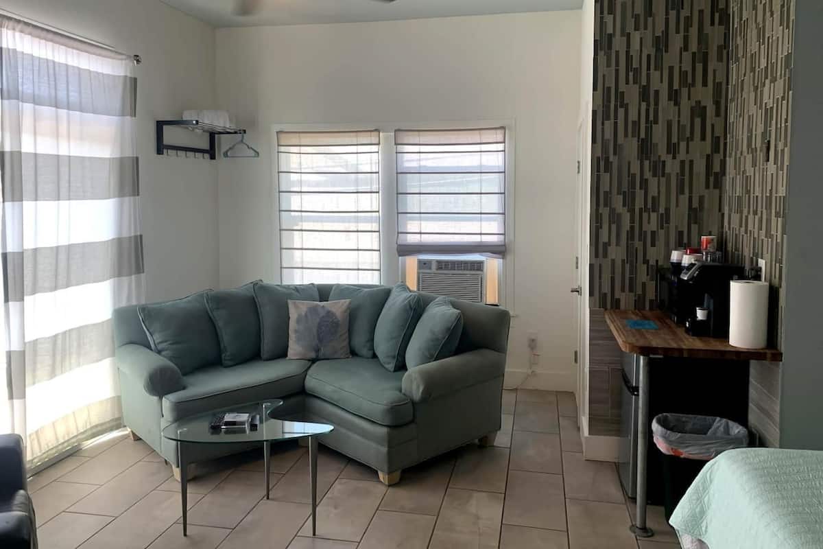 Un salon comprenant un canapé d’angle, une table basse en verre, un ventilateur de plafond et un mur décoré d’un motif.