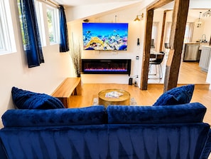 A living room with a blue sofa, a flat-screen TV, a fireplace, and a kitchen in the background.