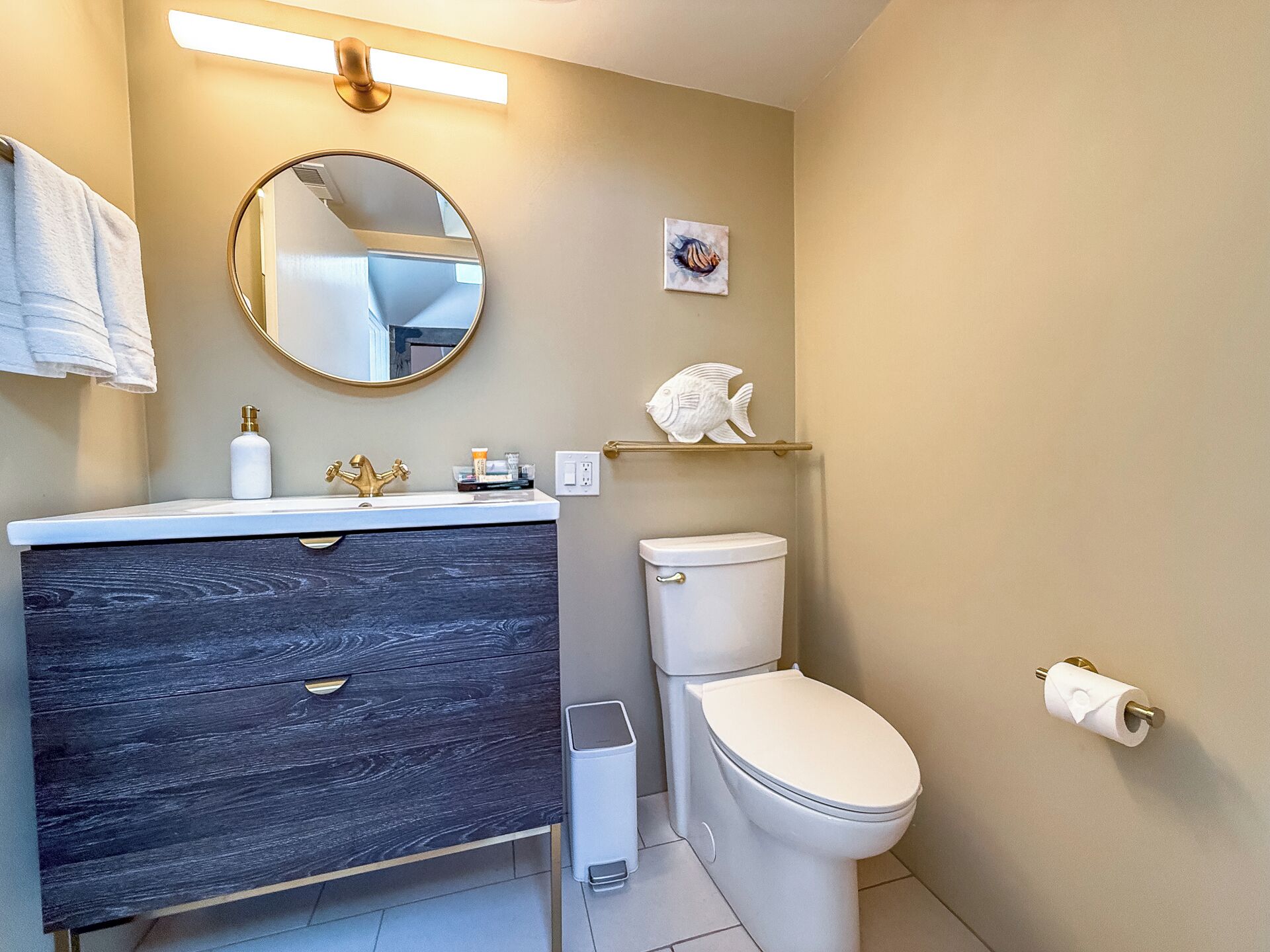 A modern bathroom with a dark wood vanity, a white toilet, and a round mirror.