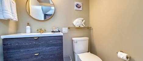 A modern bathroom with a dark wood vanity, a white toilet, and a round mirror.