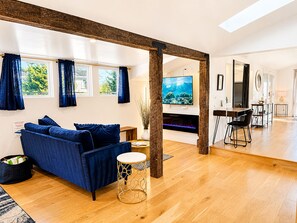 A modern living room with a blue sofa, wooden flooring, a fireplace, and a television.
