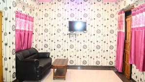 A living room with a black leather sofa, a wooden coffee table, a flat-screen TV mounted on the wall, and patterned wallpaper. - H R Paying Guest House (Varanasi)