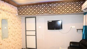 A room with a patterned wall, a television mounted on the wall, a door, and a black leather sofa. - H R Paying Guest House (Varanasi)