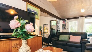 Ein Wohnzimmer mit Fernseher, einem Holzkabinett, einer gewebten Vase, einem Tisch mit Untersetzer, einer schwarzen Ledersofa und einem Bücherregal.