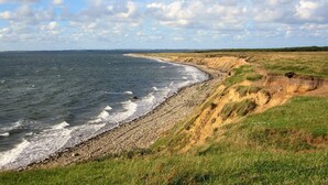Eine Küstenlandschaft mit Kiesstrand, grasbewachsenen Dünen und blauem Himmel.