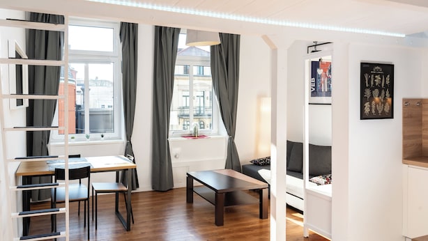 A modern room with a wooden floor, a desk with a chair, a small table, a sofa, and a window with curtains. - Cozy apartment with loft bed in Dresden Neustadt - your temporary home (Dresden)