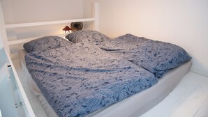 A bed with a blue patterned bedspread and pillows, a white headboard, and a small table with a lamp and a fan. - Cozy apartment with loft bed in Dresden Neustadt - your temporary home (Dresden)