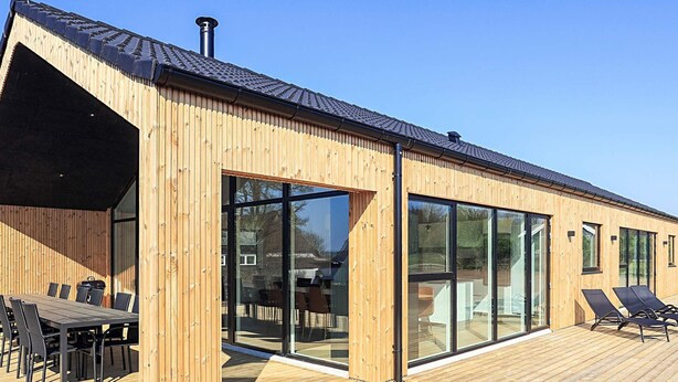 Ein modernes Holzgebäude mit großen Glasüren und einer Terrassenfläche mit Gartenmöbeln.