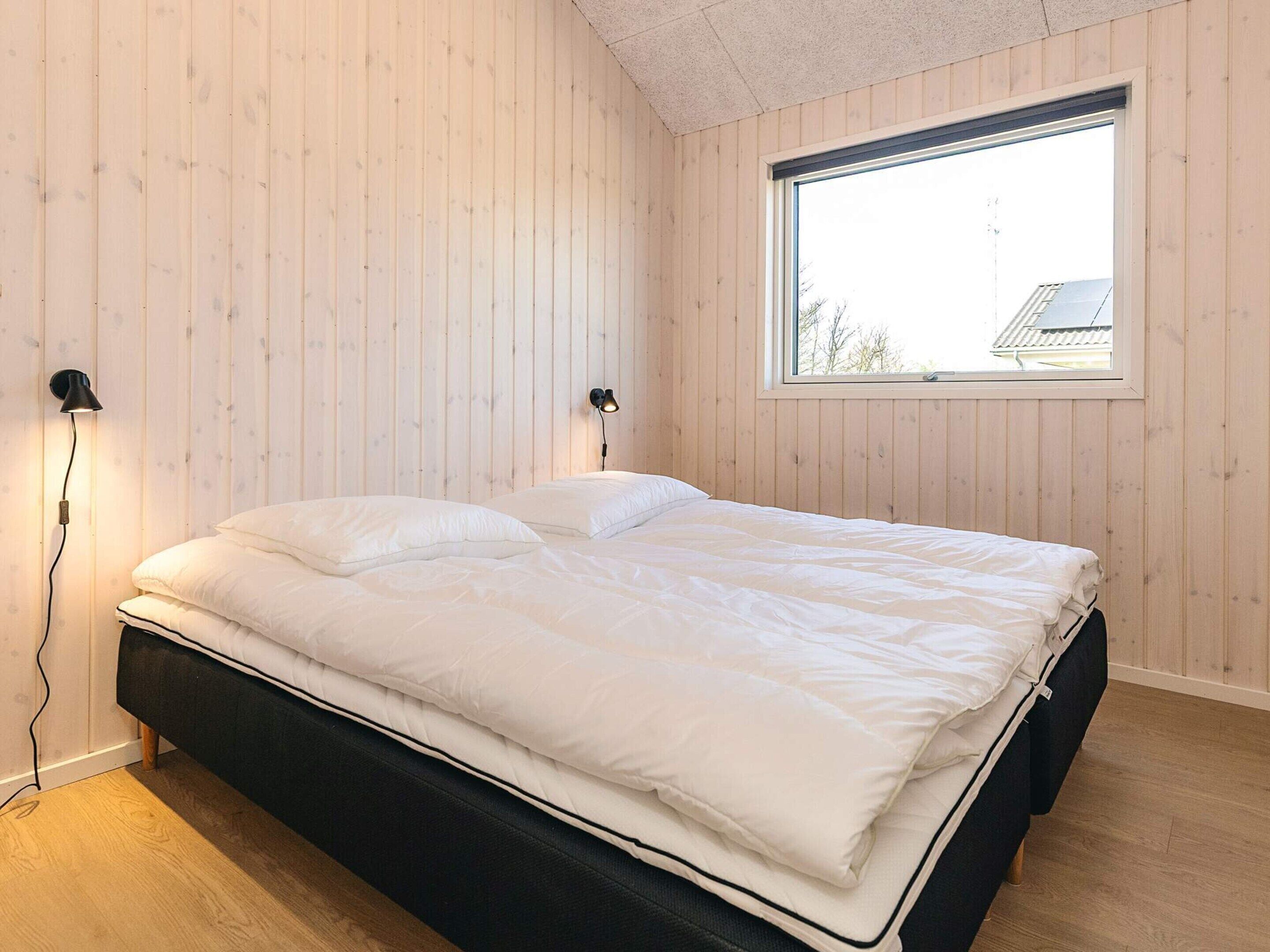 A bedroom with a bed, two bedside lamps, a window, and wooden walls.