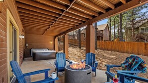 Un patio cubierto con un brasero, sillas Adirondack azules y un jacuzzi.