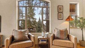 Una sala de estar acogedora con sillones de cuero, una mesita de madera y un ventanal con vistas a árboles.