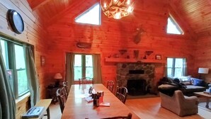 Ein gemütliches Blockhaus mit einem langen Esstisch, Holzsesseln, einem Kamin und einer Couch.