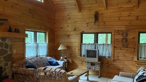 Ein gemütliches Blockhaus-Interieur mit Kamin aus Naturstein, Holzwänden, Deckenventilator und Fernseher.