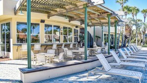 A poolside area with lounge chairs and tables, a covered seating area, and a building with large windows.