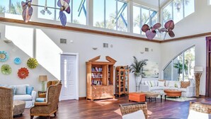 A spacious living room with high ceilings, large windows, and a variety of seating options including a sofa, chairs, and a round table.