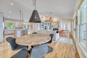 Una cocina amplia con una isla central, iluminación colgante moderna y un comedor con sillas de mimbre.