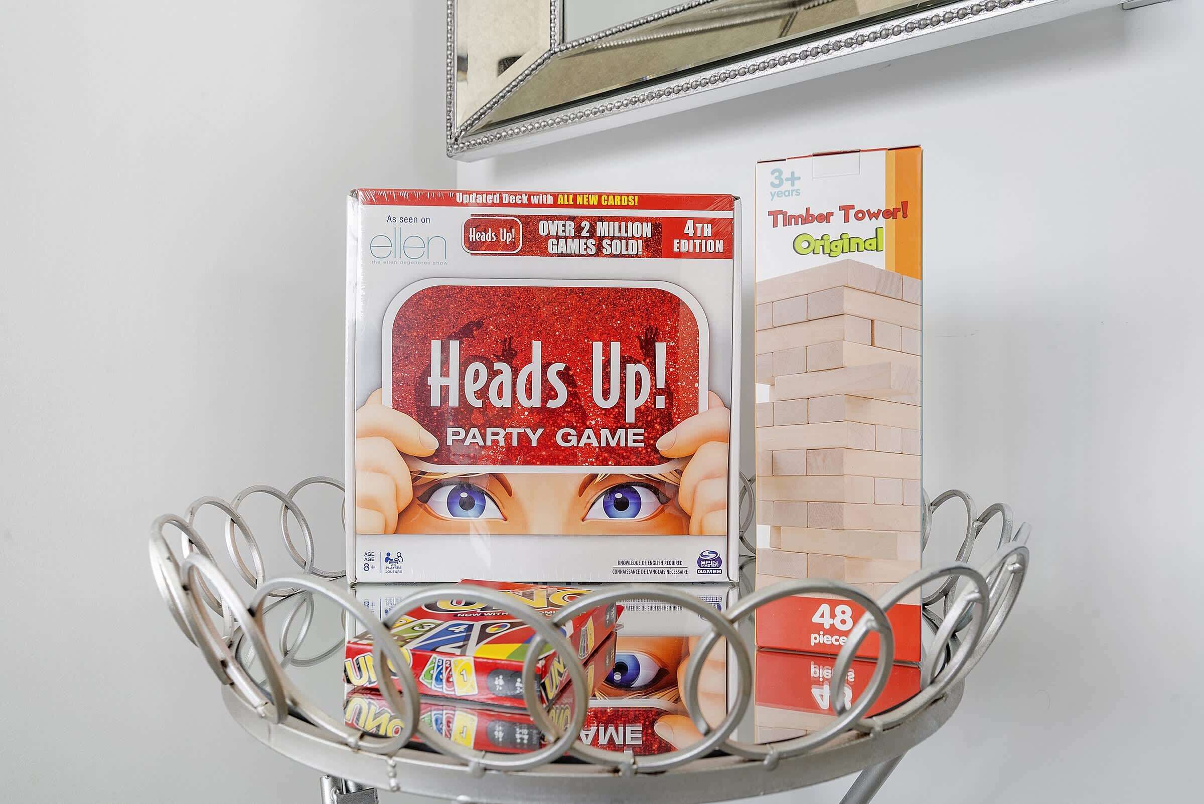 Une étagère en métal sur laquelle se trouvent un jeu de société intitulé « Heads Up! PARTY GAME » et une boîte de jeu appelée « Timber Tower ».