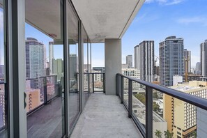 Un balcón con vistas a la ciudad, ventanas amplias y suelo de hormigón.