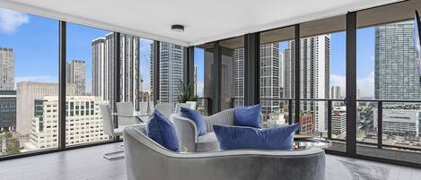 A modern living room with a grey sofa, blue cushions, and a city view through large windows.
